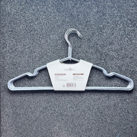 A sleek metal hanger with a durable design, featuring curved edges and a central hook, displayed with packaging instructions on a textured gray carpet background.