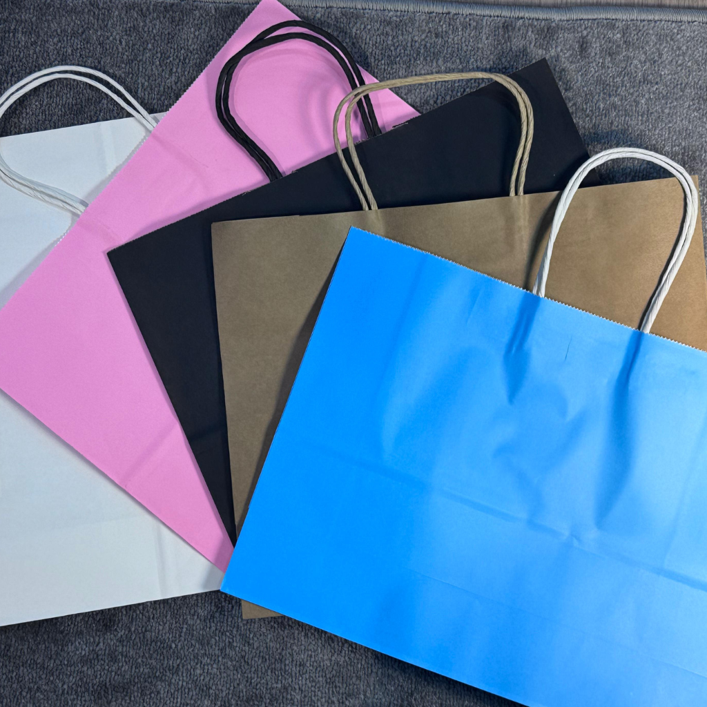 A collection of colorful A5-sized kraft paper bags with twisted handles, displayed on a gray background. Includes bags in white, pink, black, brown, and blue