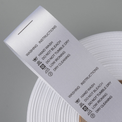 A roll of custom satin labels with printed washing instructions, designed for smooth and durable branding on garments and textiles.