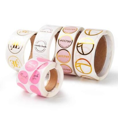 A set of custom paper sticker rolls featuring colorful and gold foil designs, available in glossy or matte lamination, perfect for branding and packaging needs.