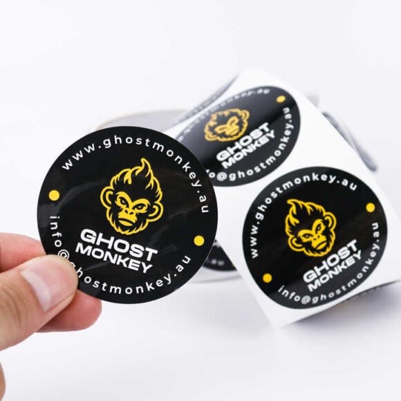 A roll of custom circular vinyl stickers featuring a bold "Ghost Monkey" logo with glossy lamination, perfect for branding and promotional use.